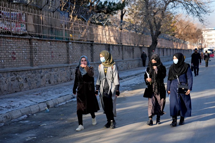 Four people walking in a street, all of them wearing head coverings, and three of four wearing face coverings.