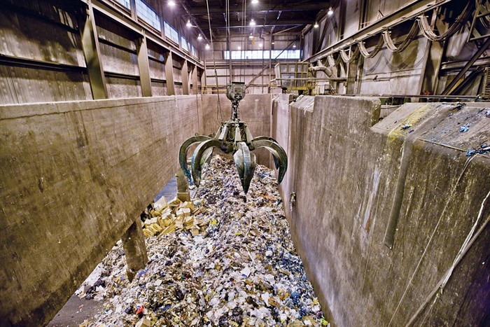 A photo of large steel claws agitating garbage in a large, indoor trench.