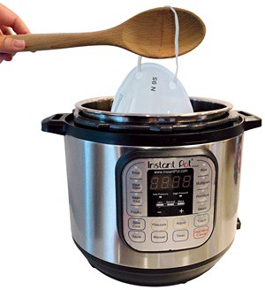 An image of an N95 mask being lifted out of an Instant Pot with a wooden spoon. 09828-newscripts-pot.jpg